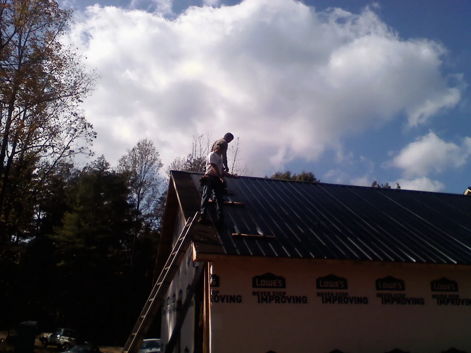 Roofer fastening dark metal panels high against a cloudy sky, from a Roof Inspection job in Miami